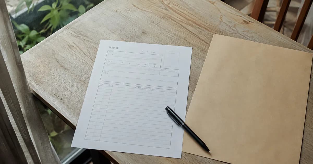 明るい木の机に置かれた白い書類、黒いペンと封筒